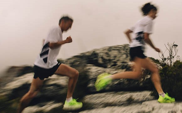 Two people running on a dirt path surrounded by lush vegetation in the background.