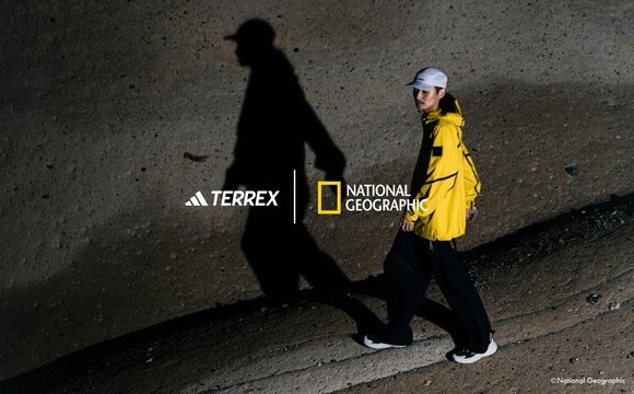 A person wearing a yellow jacket and a white helmet stands on a rocky terrain, with their shadow cast on the ground.