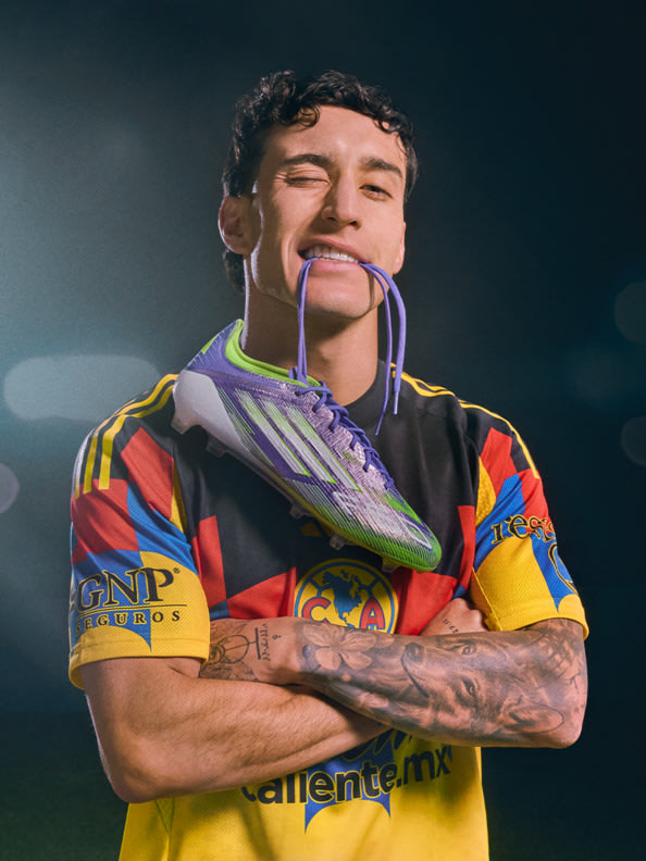 A person with tattoos and a colorful, patterned jersey is standing with their arms crossed, appearing to be in a sports or athletic setting.