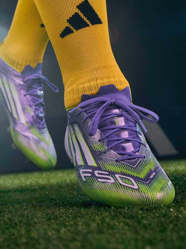 The image shows a pair of colorful athletic shoes with yellow socks on a grassy field.