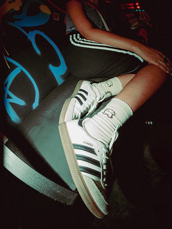 The image shows a pair of white and green Adidas sneakers resting on a colorful, graffiti-covered surface.