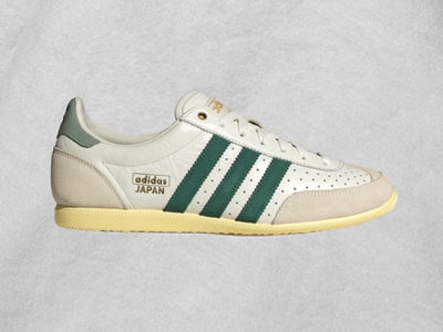 A pair of white and green Adidas Japan sneakers with a perforated leather upper and a gum sole, set against a plain gray background.