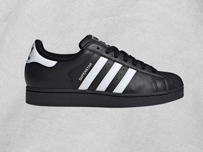 A black and white Adidas Superstar sneaker with three white stripes on a plain background.