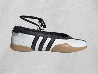 A black and white athletic shoe with a beige sole and laces against a plain, light-colored background.