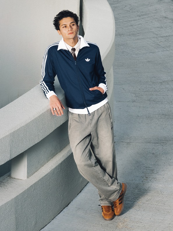 A young person wearing a navy blue jacket with white stripes, standing in front of a white wall.
