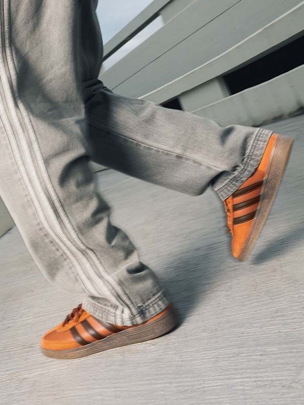 The image shows a person's legs and feet wearing gray pants and bright orange sneakers, with the feet in motion against a blurred background.