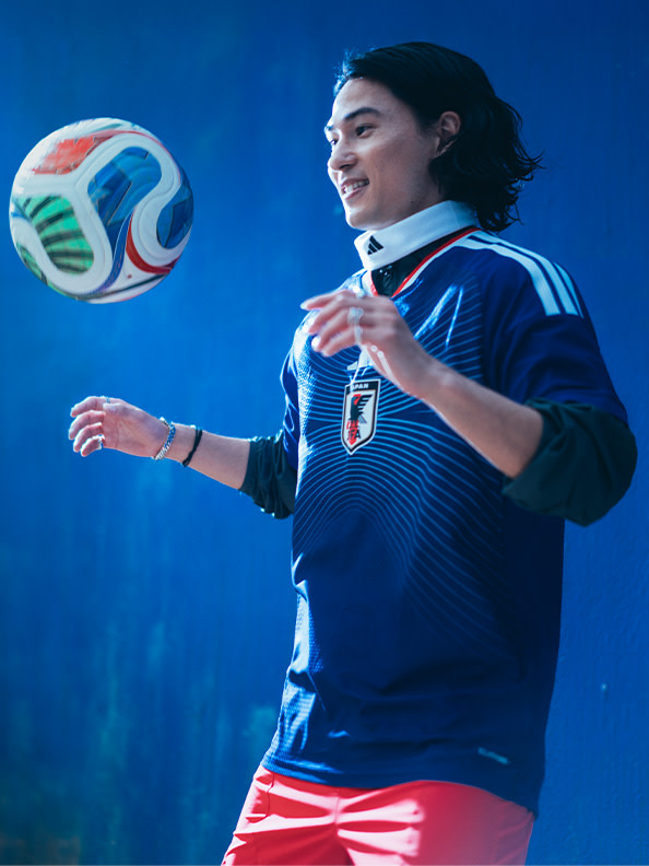 A person in a blue sports jersey is juggling a soccer ball against a vibrant blue background.