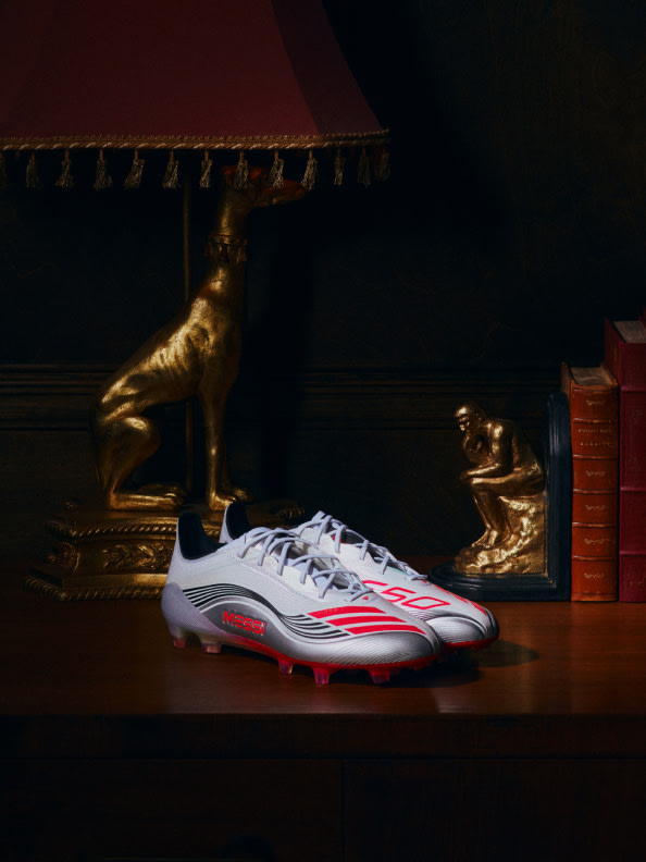 The image features a pair of white and red athletic shoes in the foreground, with a golden statue and books visible in the background, creating an intriguing contrast between the modern and the ancient.
