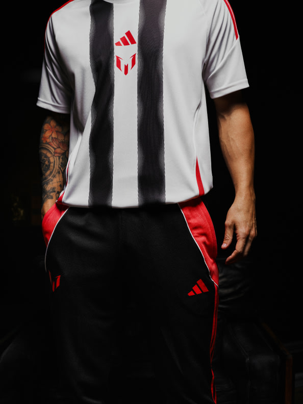 A white and red sports jersey with the Adidas logo, worn by a person with tattoos on their arms, against a dark background.