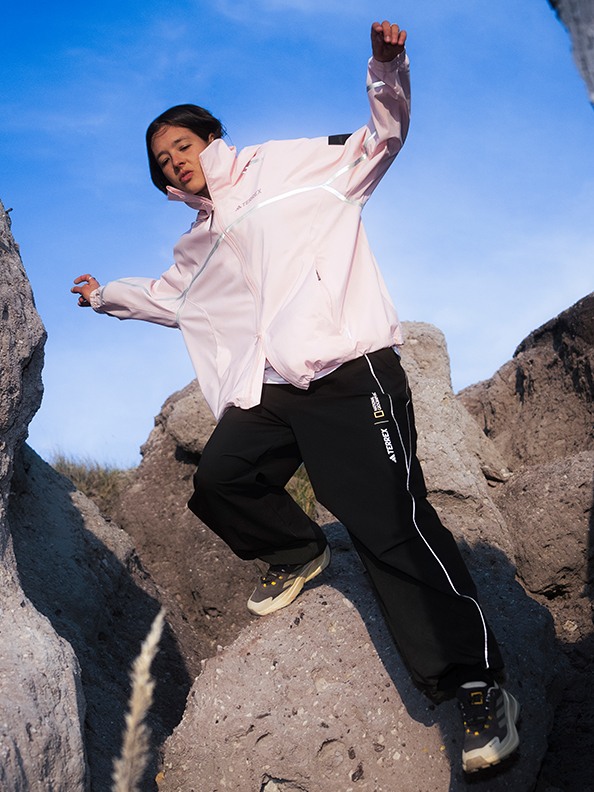 A person in a white shirt and black pants is jumping in the air against a backdrop of rocky terrain and a clear blue sky.