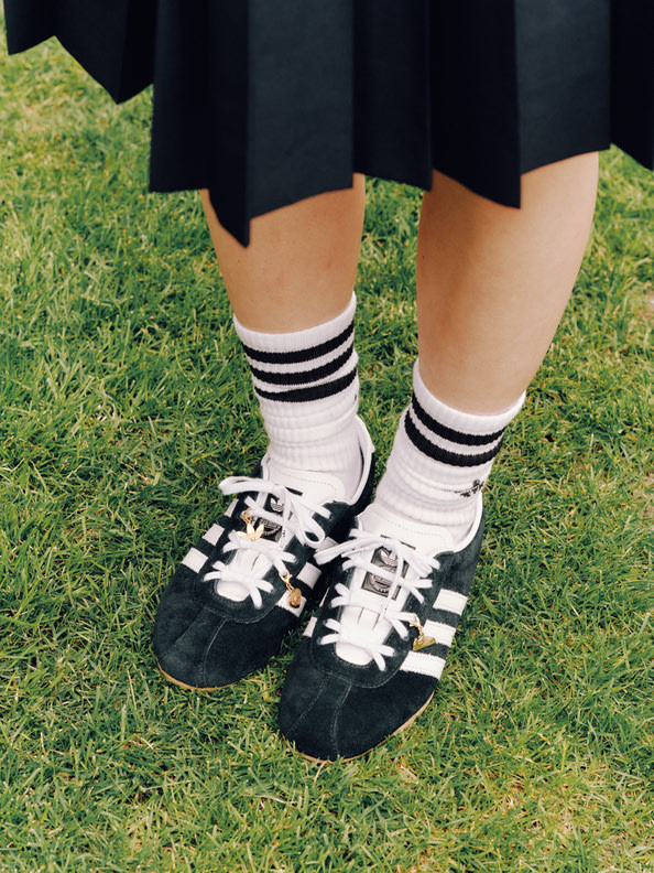 The image shows a person's legs and feet standing on grass, wearing black and white striped socks and black and white patterned shoes.