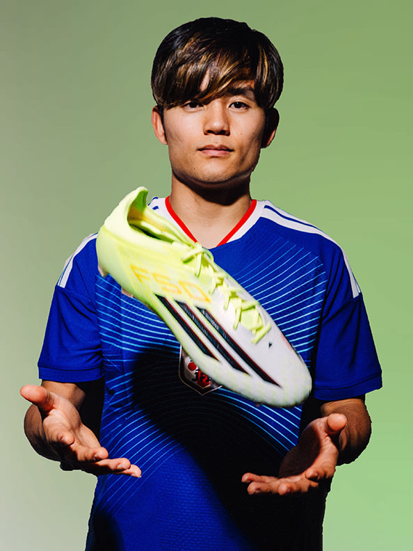 A young man wearing a blue sports jersey and holding a yellow soccer cleat stands in front of a green background.