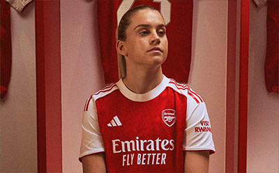 The image shows a young man wearing a red and white soccer jersey with the "Emirates Fly Better" logo, standing in front of a red and white striped background.