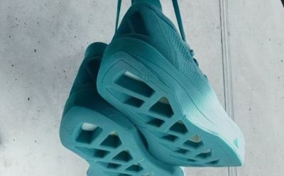 A teal-colored, lightweight and breathable athletic shoe with a perforated upper design, hanging against a plain, light-colored background.