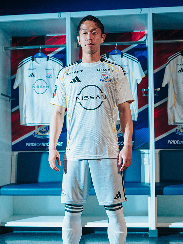 A young man wearing a white soccer jersey with the Nissan logo stands in front of a locker room display showcasing various jerseys and equipment.