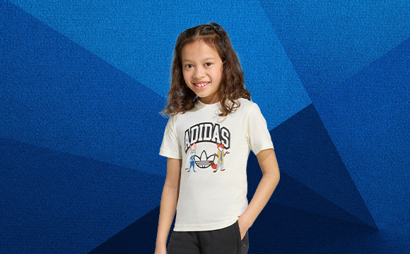 A young girl with curly hair is smiling and wearing a white t-shirt with a graphic design on a vibrant blue background.