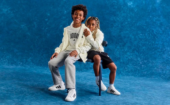 Two individuals, a man and a woman, are seated together on a blue background. The man is wearing a white sweatshirt and the woman is wearing a white top. They appear to be posing for a photograph.