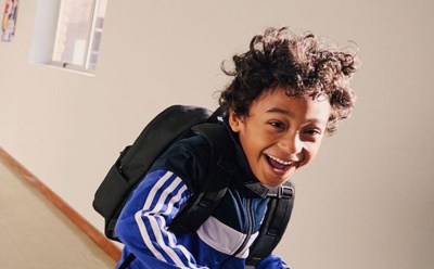 A smiling person with curly hair wearing a blue and white striped jacket stands in a room with framed artwork on the walls.