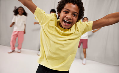 A young person in a yellow shirt is enthusiastically raising their arms, surrounded by other people in the background.