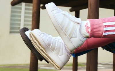 A pair of white sneakers with pink laces sit on a wooden chair against a blurred background.