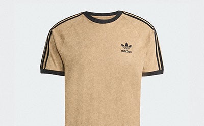 A beige and black Adidas t-shirt with the brand's iconic three-stripe design on the sleeves against a plain white background.