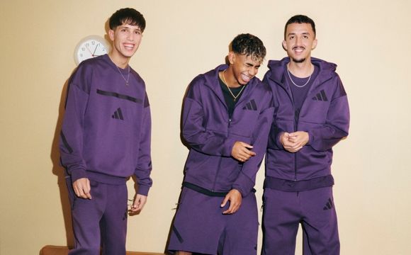 Three young men wearing matching purple hooded jackets and pants are standing together against a plain beige background.