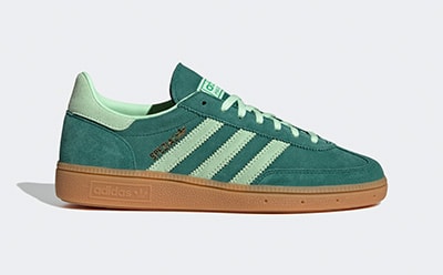 A pair of green and white Adidas sneakers with a gum sole sits on a plain white background.