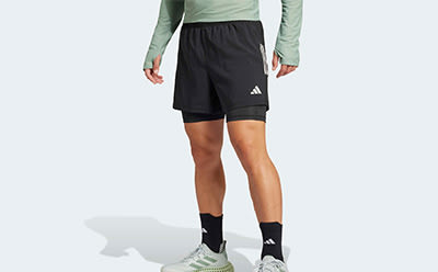 The image shows a person wearing black athletic shorts and white and black sneakers, standing against a plain background.