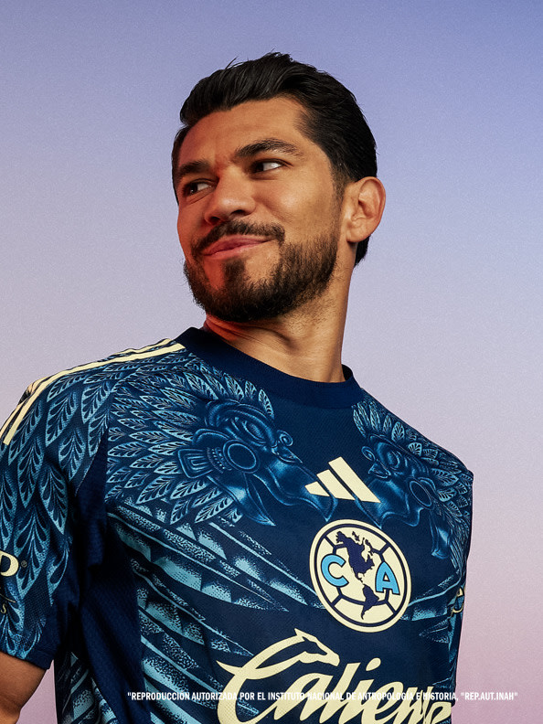 The image shows a man wearing a blue and white patterned sports jersey, with a logo on the front, against a clear blue sky background.