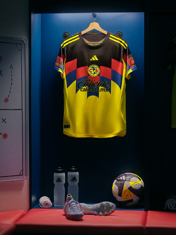 A yellow and red soccer jersey hangs on a rack, accompanied by a soccer ball and cleats, set against a dark blue background.