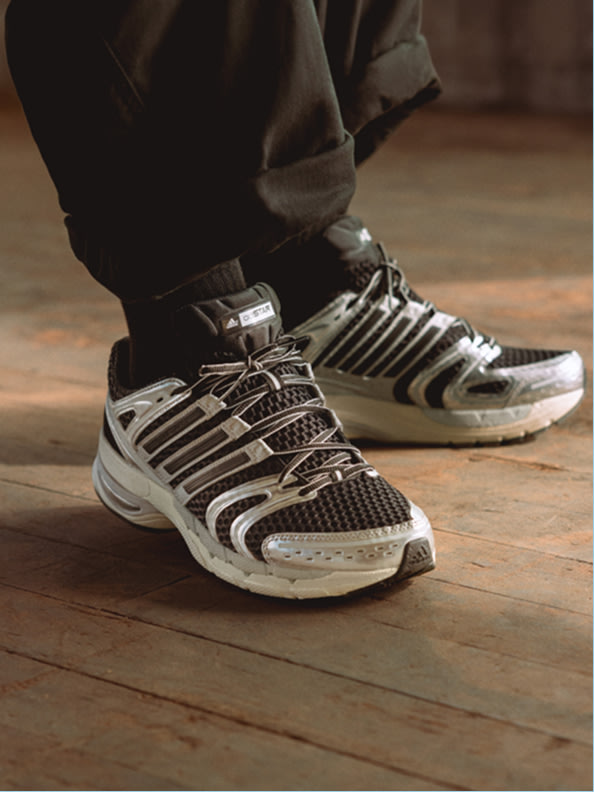 The image shows a pair of black and white athletic shoes on a wooden floor, with the person's legs visible in the foreground.