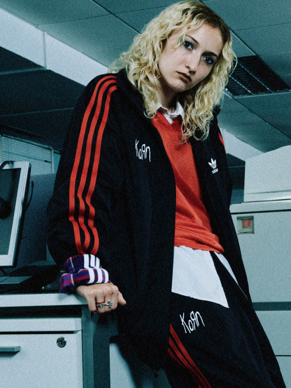 This image depicts a model in the adidas Originals x KoRn track top, standing out in an office environment.