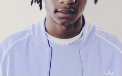 A man with black hair wearing a lavender adicolor tracksuit pictured from the neck up.