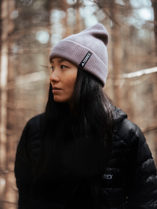Eine Person, die eine graue Mütze und eine schwarze Winterjacke trägt, steht in einem Waldgebiet mit verschwommenen Bäumen im Hintergrund.