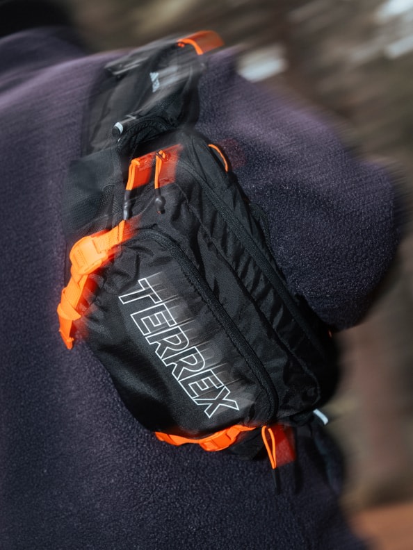 Ein schwarz-orangefarbener Rucksack mit dem Aufdruck „Therrey“ auf einem dunklen, verschwommenen Hintergrund.