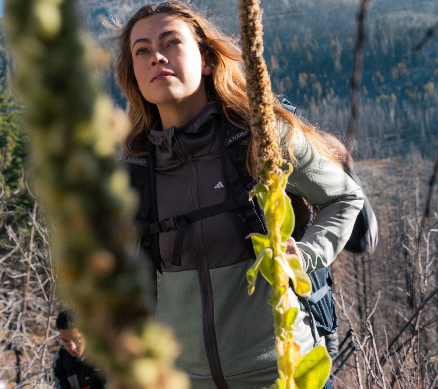 An image of a woman wearing items from the new TERREX SS24 range, stooped down over a stream in a forest, splashing his face with water.