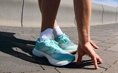 The image shows a pair of colorful sneakers, with a mint green and white color scheme, resting on a paved surface against a backdrop of a clear sky.