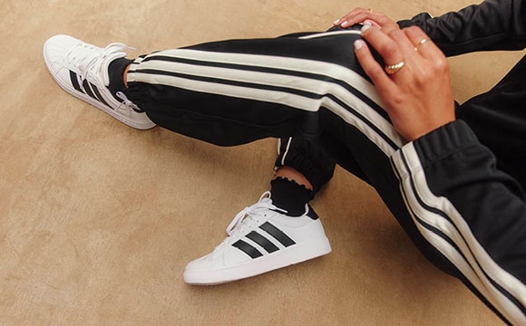 The image shows a person's lower body wearing black and white striped pants and white sneakers, standing on a beige surface.
