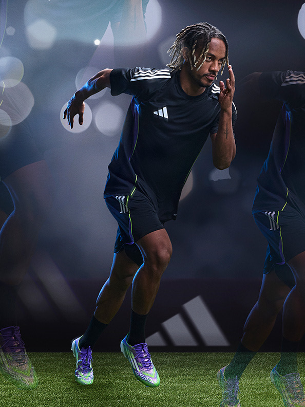 A person wearing a black athletic outfit is crouched down on a grassy field, with a blurred background of stadium lights and spectators.