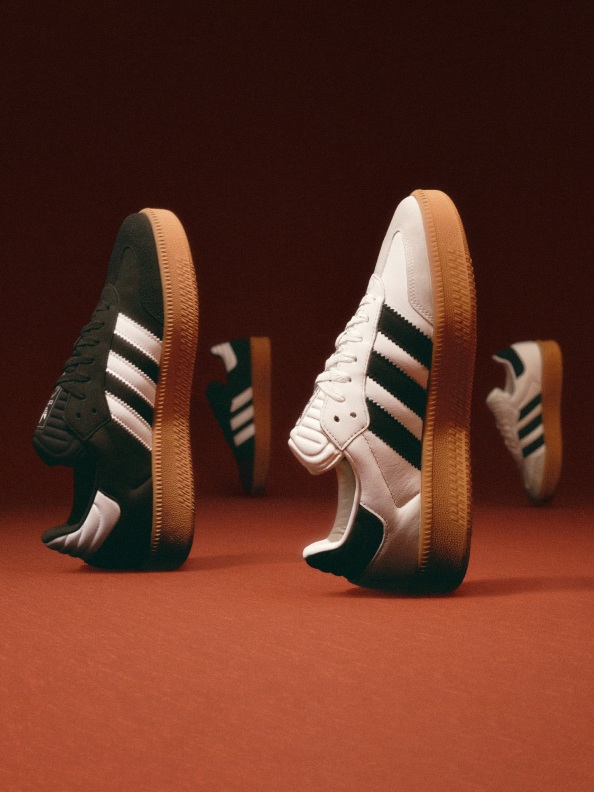 The image shows a pair of white and green sneakers with gum soles against a dark brown background.
