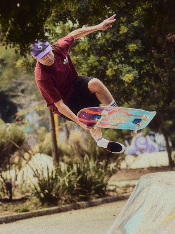 A person in a red shirt is performing a skateboarding trick in a lush, green outdoor setting.
