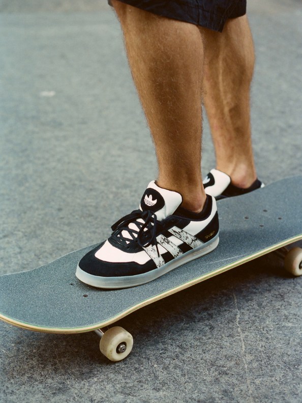 A person's legs and feet are visible, wearing black and white sneakers while standing on a skateboard on a concrete surface.