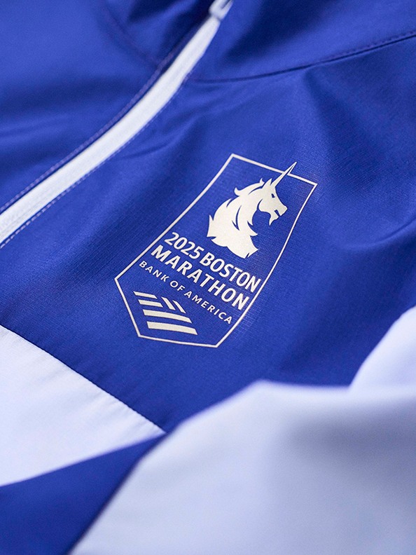 The image shows a close-up view of a blue athletic jacket with the logo of the Boston Marathon prominently displayed on the front.
