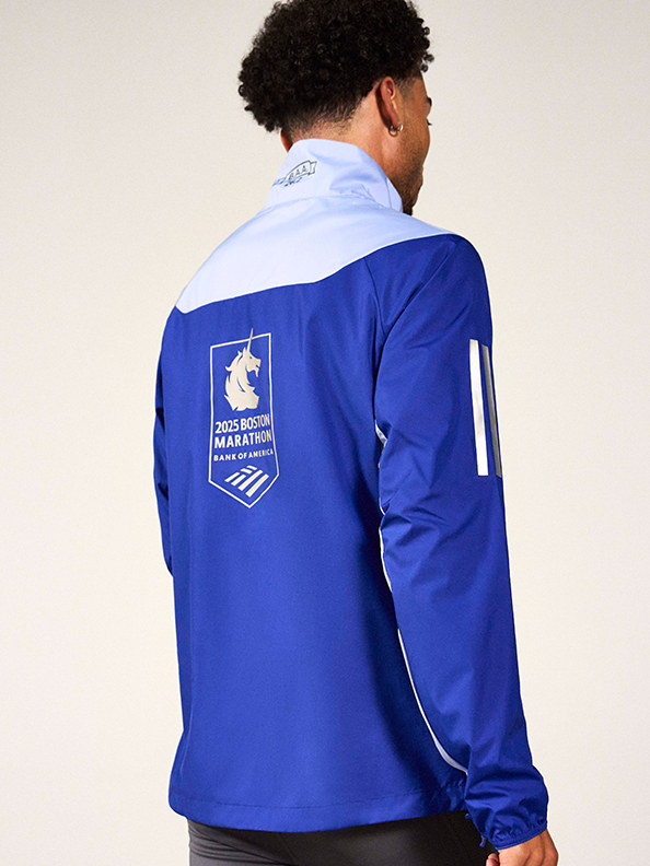 A person wearing a blue jacket with a logo on the back, standing against a plain background.
