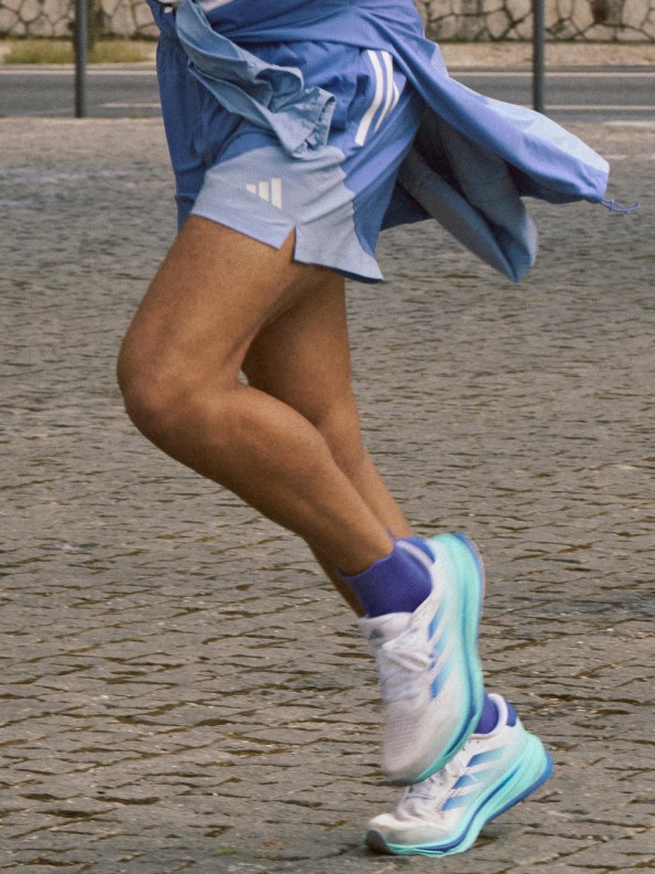 A man running outdoors in light blue shorts and adidas Supernova shoes, pictured from the waist down.