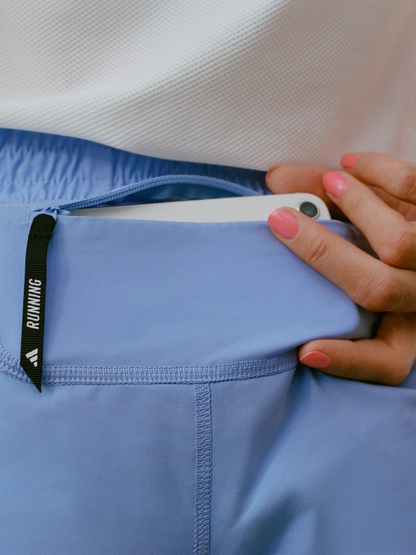 A close-up of a mobile phone placed into the pocket of a pair of light blue adidas Supernova running leggings. 
