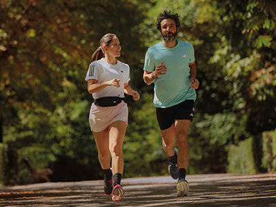 Two people, a man and a woman, are jogging together on a path surrounded by lush greenery and trees.