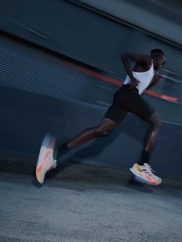 A man running on road, blurred in motion, wearing the Adizero Boston 12.