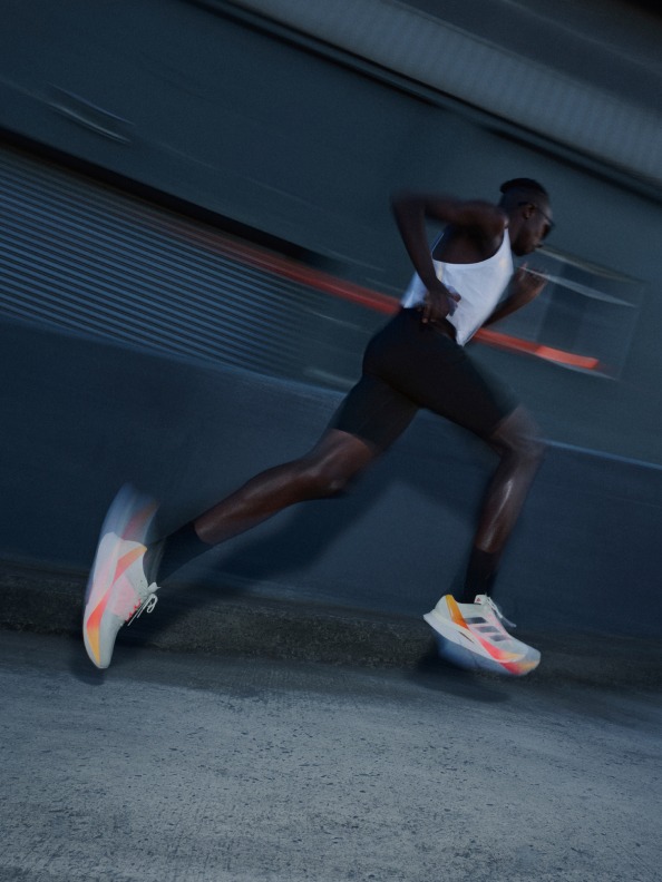 A man running on road, blurred in motion, wearing the Adizero Boston 12.