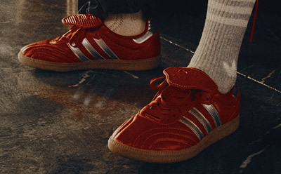 A pair of red and white sneakers with laces, resting on a wooden surface with a dark background.